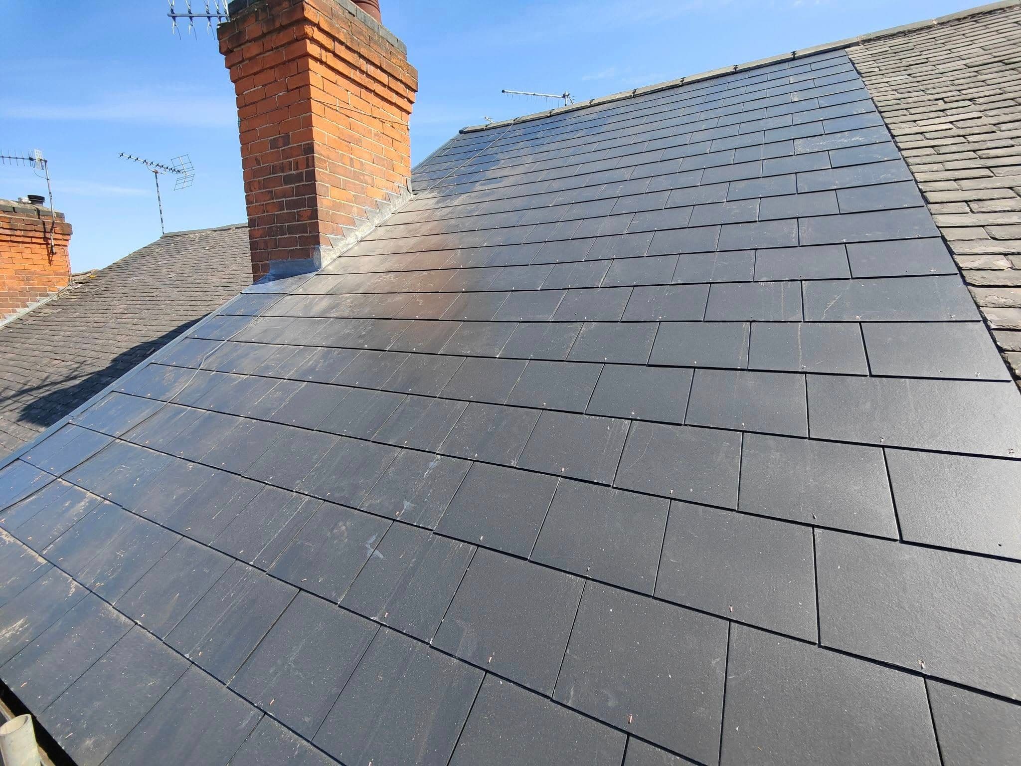 Finished slate roof laid tightly around a brick chimney stack