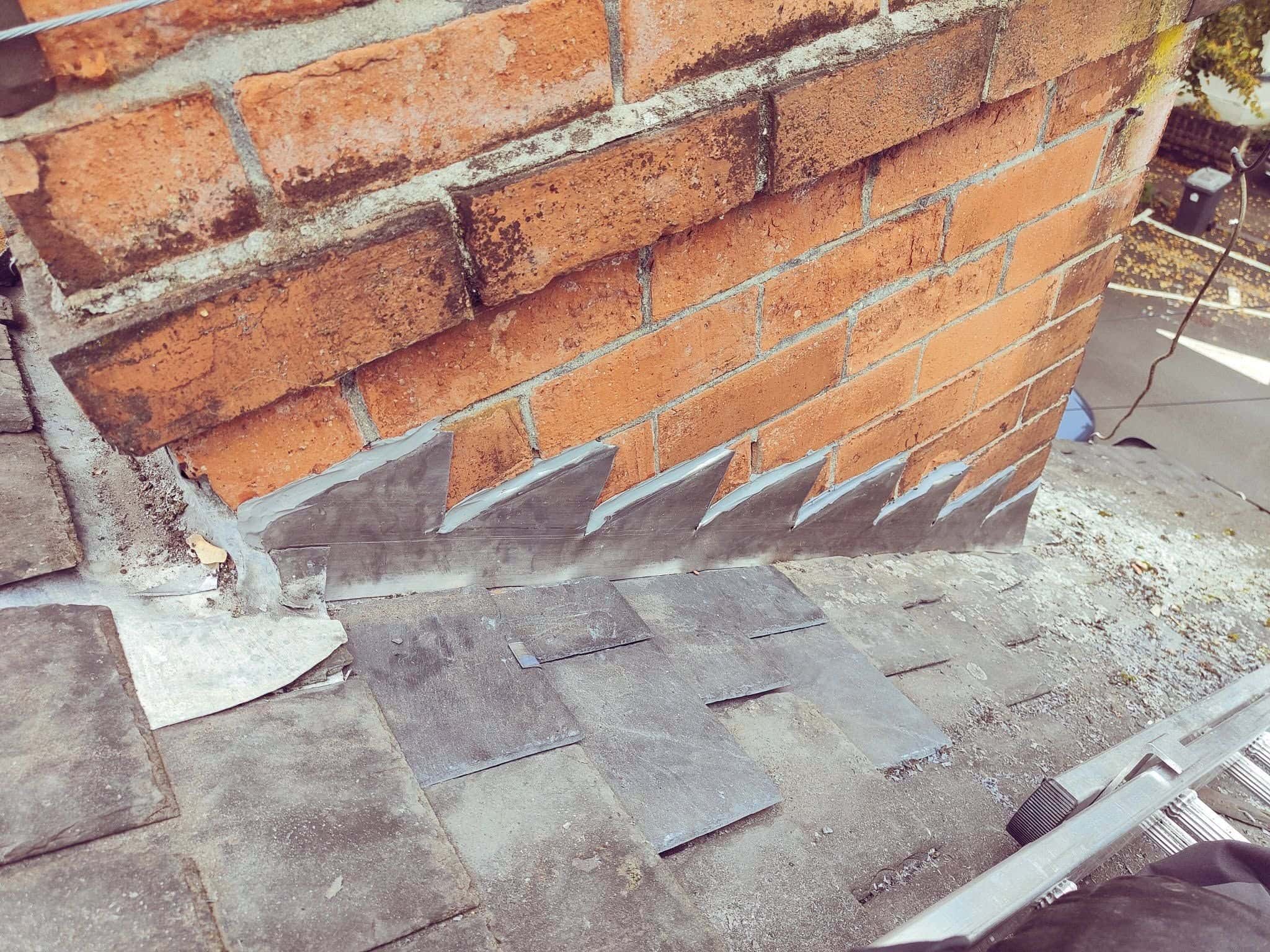 New lead flashing fitted between slate tiles at the base of a chimney stack